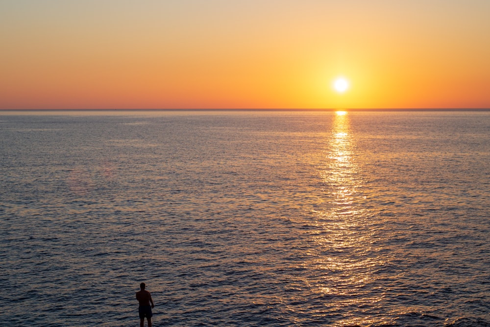 eine Person, die an einem Strand steht und den Sonnenuntergang beobachtet