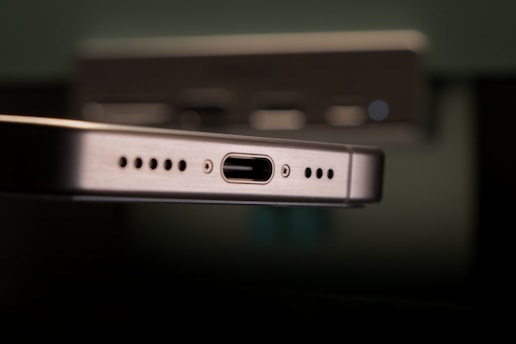 Close-up of a metallic device featuring a USB-C port flanked by speaker grills. The focus is sharp on the port while the background is blurred, suggesting an emphasis on technology and connectivity.