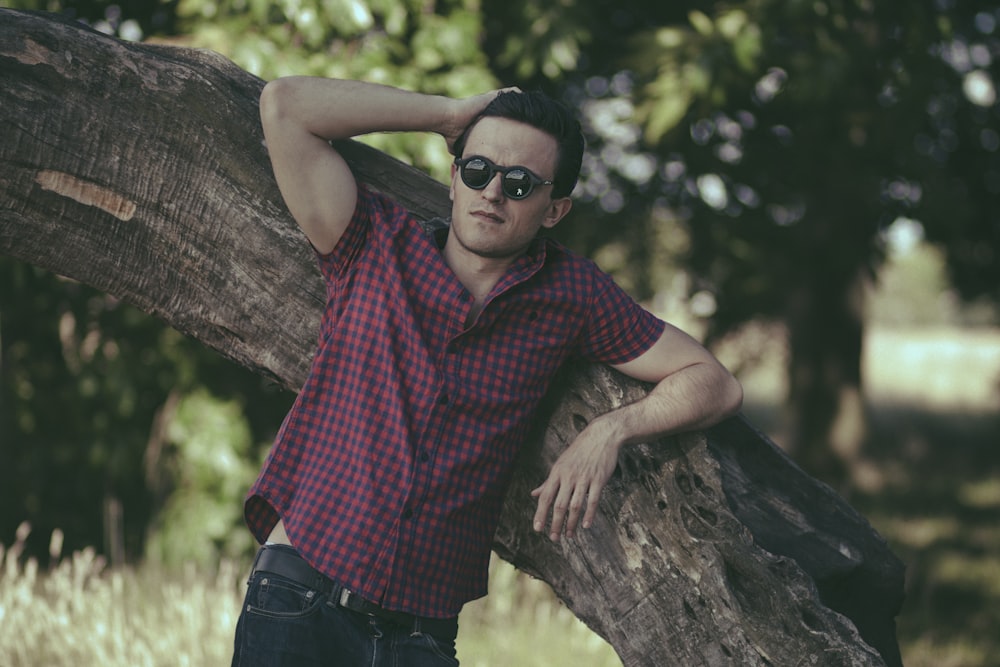 a man leaning on a tree trunk wearing sunglasses