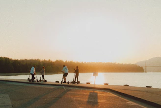 A group of diverse people riding electric scooters through a vibrant city street at sunset.