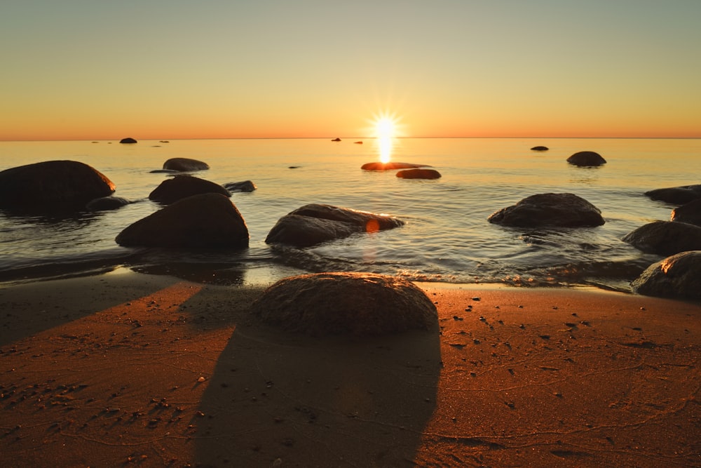 Die Sonne geht über dem Ozean mit Steinen im Wasser unter