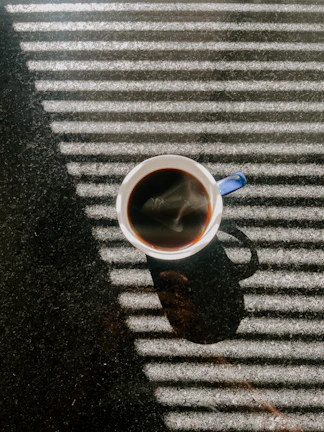 Close-up of a colorful tumbler filled with freshly brewed coffee, sunlight highlighting its texture.