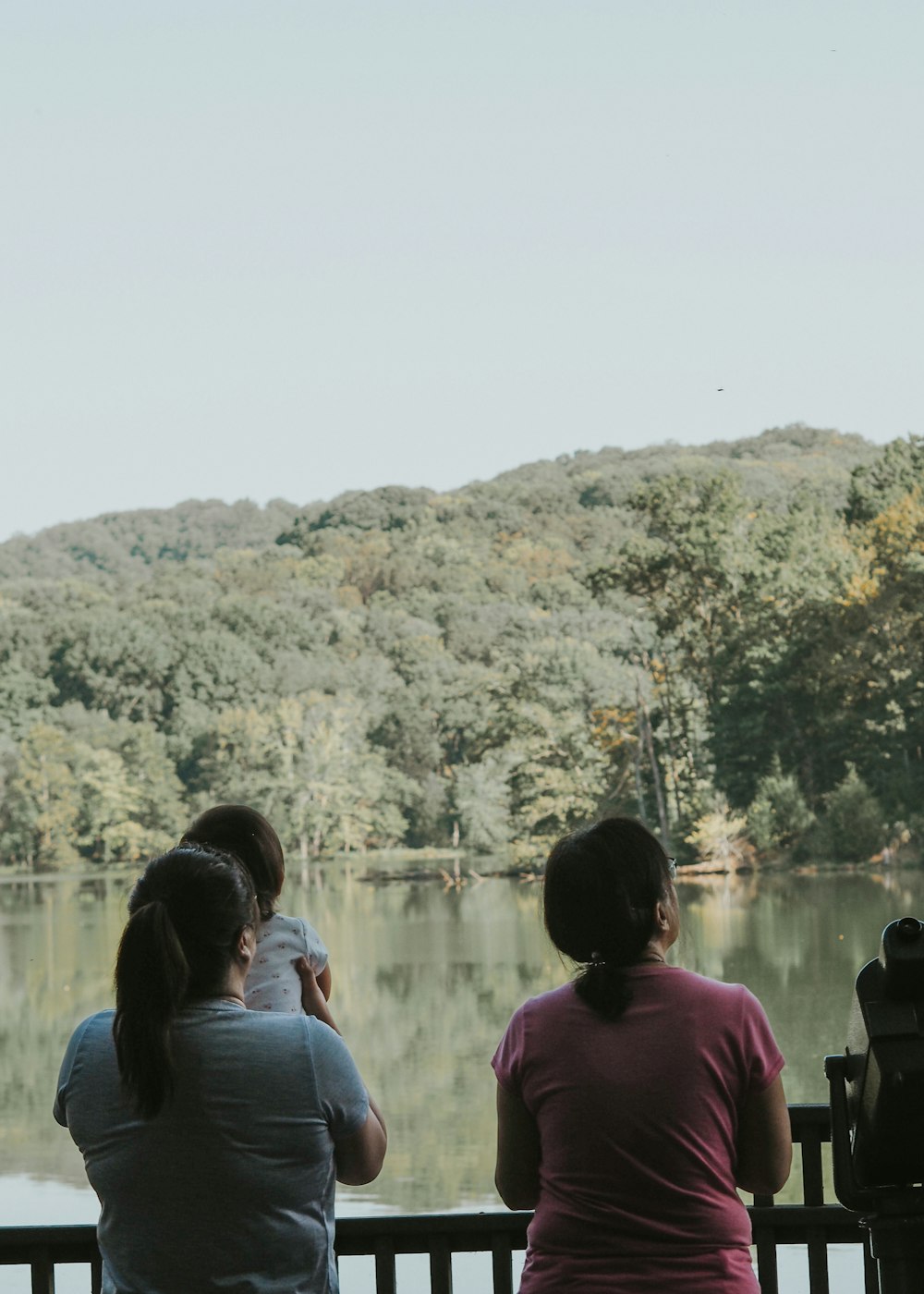 three people sitting on a bench looking at a lake