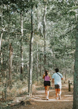 A runner and a walker on a forest trail, smiling and enjoying the outdoors.