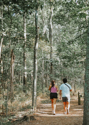 A runner and a walker on a forest trail, smiling and enjoying the outdoors.