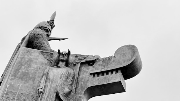 An intricate sculpture featuring a knight or warrior wearing a helmet and chainmail, holding a spear. Below, an angelic figure with wings and a shield is prominently carved. The style is reminiscent of medieval or gothic art, with detailed craftsmanship.