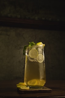 A vibrant glass of fresh lemon juice with slices of lemon and a sprig of mint on a rustic wooden table.