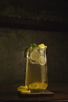 A vibrant glass of fresh lemon juice with slices of lemon and a sprig of mint on a rustic wooden table.