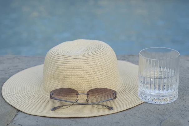 A stylish straw hat resting on a wooden deck chair beside a sparkling pool.