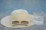Close-up of stylish sunglasses resting on a straw hat beside a tropical drink.