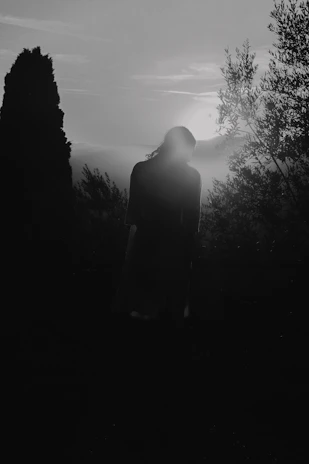 A shadowy figure standing near a forgotten stone monument at twilight.