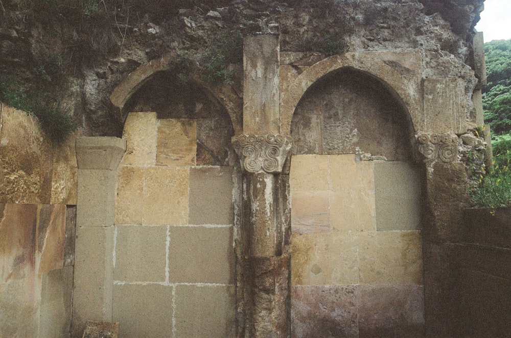 a stone wall with two archways and a clock on it