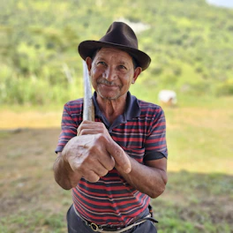 Elderly man in hat holding a tool outdoors