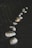 A series of oyster shells hanging above a flowing stream, suspended by strings. The shells are arranged in a line, with varying shades of iridescent white and beige. The water below is dark, emphasizing the contrast with the lighter tones of the shells.