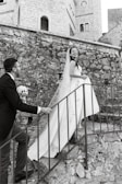 Bride and groom laughing together on a sandstone staircase, framed by intricate Jaipuri patterns.