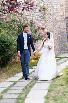 Bride and groom walking hand in hand along a sunlit path.