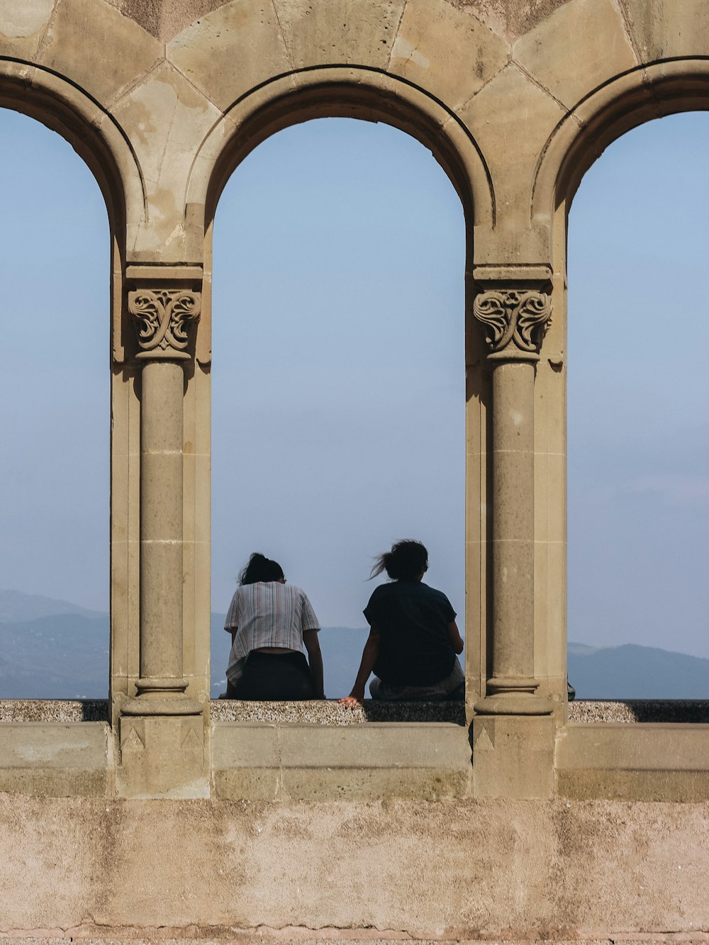 a couple of people sitting on top of a stone wall