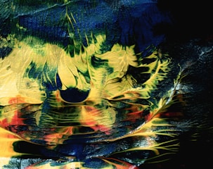 A textured and abstract composition featuring swirling patterns of green, blue, yellow, and red. The colors blend together, creating shapes that resemble nature-inspired forms or surreal landscapes. The paint appears layered and dynamic, with a glossy finish reflecting light.