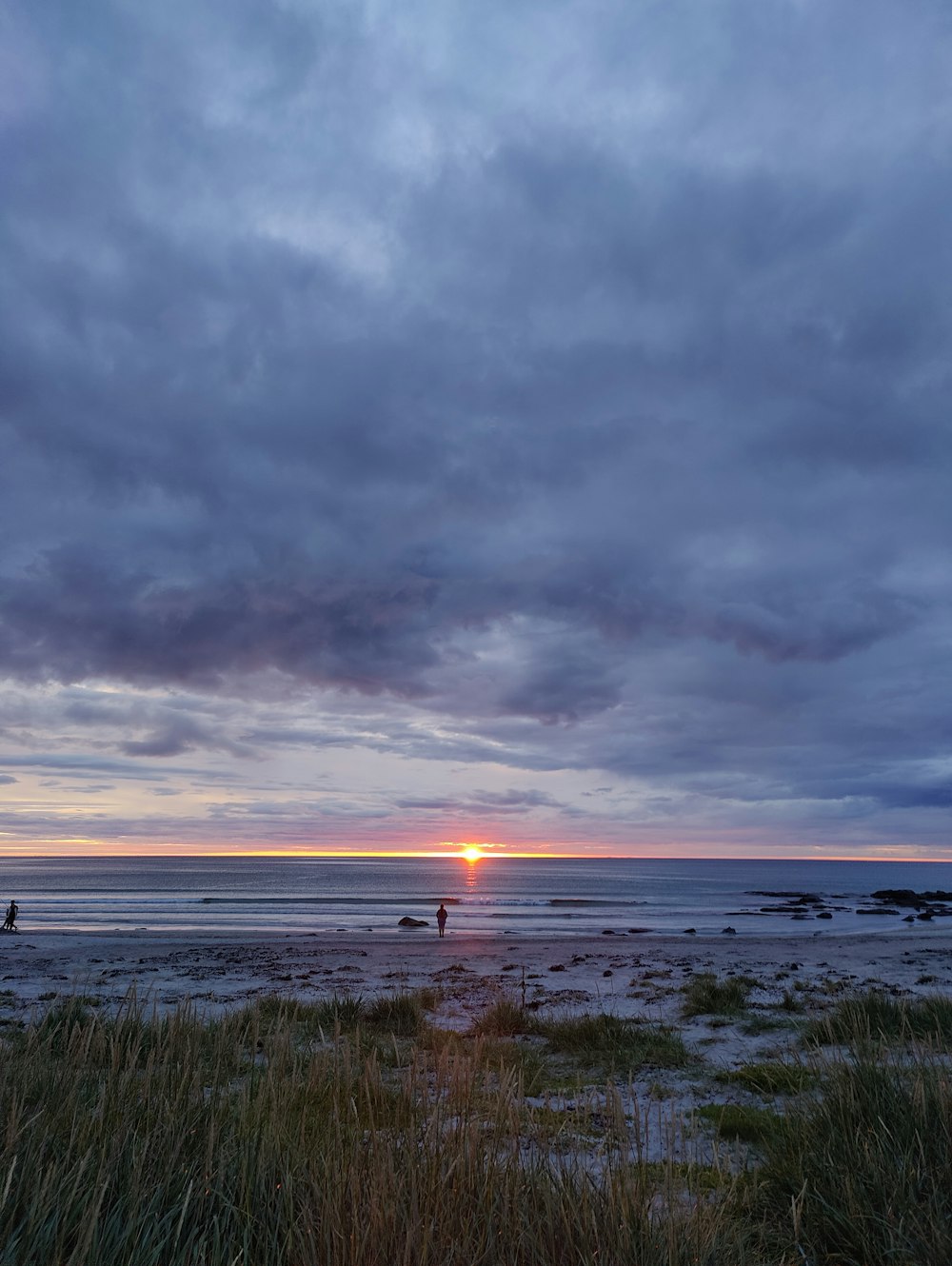 a couple of people walking on a beach under a cloudy sky