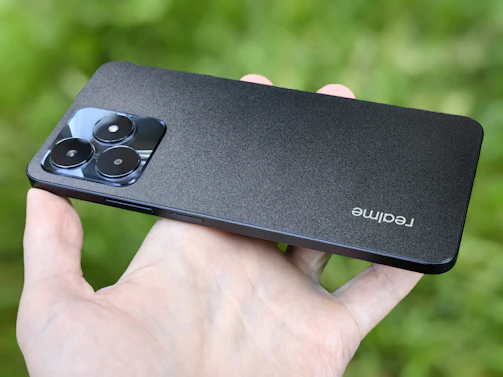 A sleek smartphone held by a hand, showcasing its triple rear camera setup against a blurred nature background.