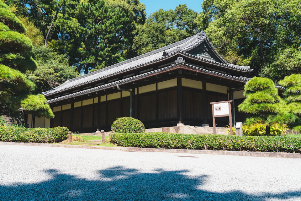 The image depicts a traditional Japanese temple nestled within a lush garden setting. The temple, painted in black and white, stands out against the verdant backdrop. Its roof is adorned with a tiled pattern that adds to its architectural charm. The temple's entrance is marked by a signpost, inviting visitors to explore further into the grounds.

The garden surrounding the temple is a symphony of nature, featuring an array of trees and bushes in various shades of green. These natural elements create a serene atmosphere, enhancing the overall aesthetic appeal of the scene. The image captures this harmonious blend of architecture and nature, offering a glimpse into the rich cultural heritage of Japan.