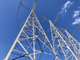 Close-up of engineers inspecting high-voltage transmission towers against a clear blue sky.