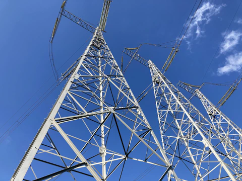 Close-up of engineers inspecting high-voltage transmission towers against a clear blue sky.