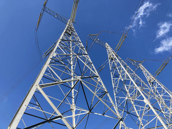 Construction workers assembling a high-voltage transmission tower under a clear blue sky.