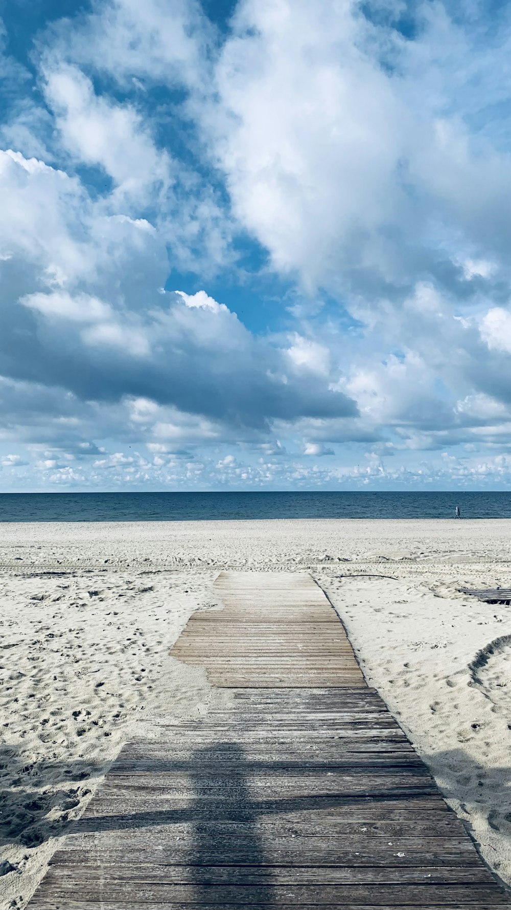 a wooden walkway leading to the ocean under a cloudy blue sky