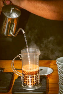 Illustration of a French press with coffee grounds and hot water being poured in, showing the steeping process.