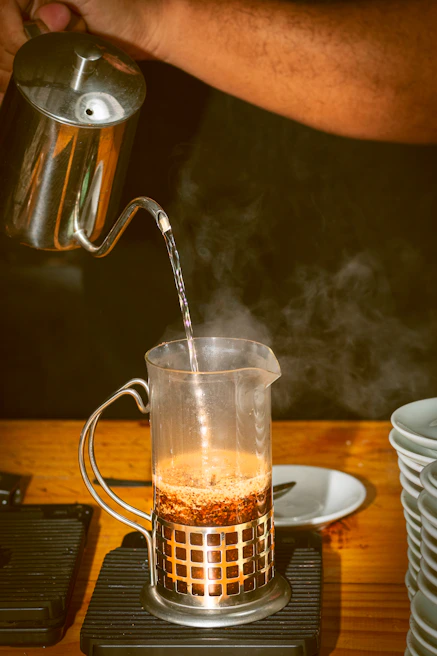 Illustration of a French press with coffee grounds and hot water being poured in, showing the steeping process.
