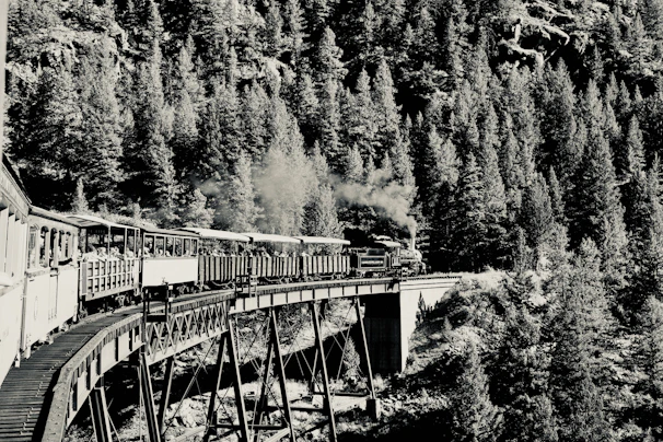 An archival photo of a vintage train crossing a steel bridge over a river.