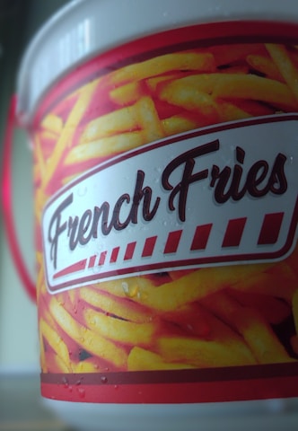 A close-up view of a container featuring an image of yellow french fries against a vibrant red background. The word 'French Fries' is prominently displayed in a bold, stylized font. The container has a glossy finish with visible droplets, suggesting condensation.