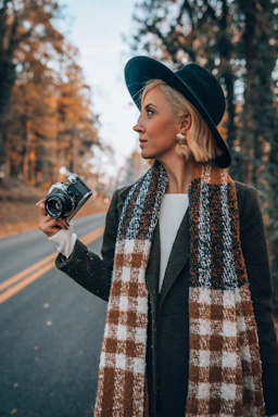 A model wearing a stylish wool fedora outdoors on a crisp autumn day with colorful leaves in the background.