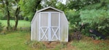 Gardeners sharing tools and chatting near a wooden shed surrounded by greenery.