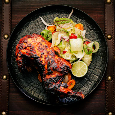A colorful plate featuring grilled chicken with fresh salad and a side of sauce, presented on a rustic wooden table.