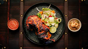 Tandoori chicken on a black plate with onion salad and chutneys