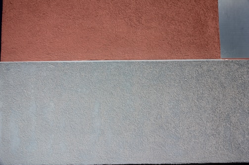 A textured surface divided into two large sections, with the upper part in a reddish-brown hue and the lower section in a grayish-blue color. The textures appear rough and uneven, suggesting a stucco or plaster finish.