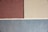 Three sections of textured wall in shades of brown, beige, and blue are separated by white lines. The top left section is brown, the top right is beige, and the bottom section is a cool blue. The texture appears to be plastered, giving a rough and natural finish.