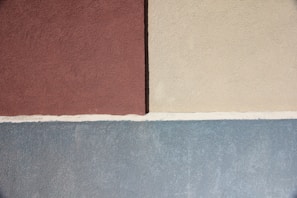 Three sections of textured wall in shades of brown, beige, and blue are separated by white lines. The top left section is brown, the top right is beige, and the bottom section is a cool blue. The texture appears to be plastered, giving a rough and natural finish.