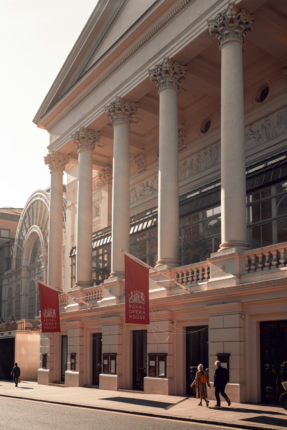 a large building with columns and people walking on the sidewalk