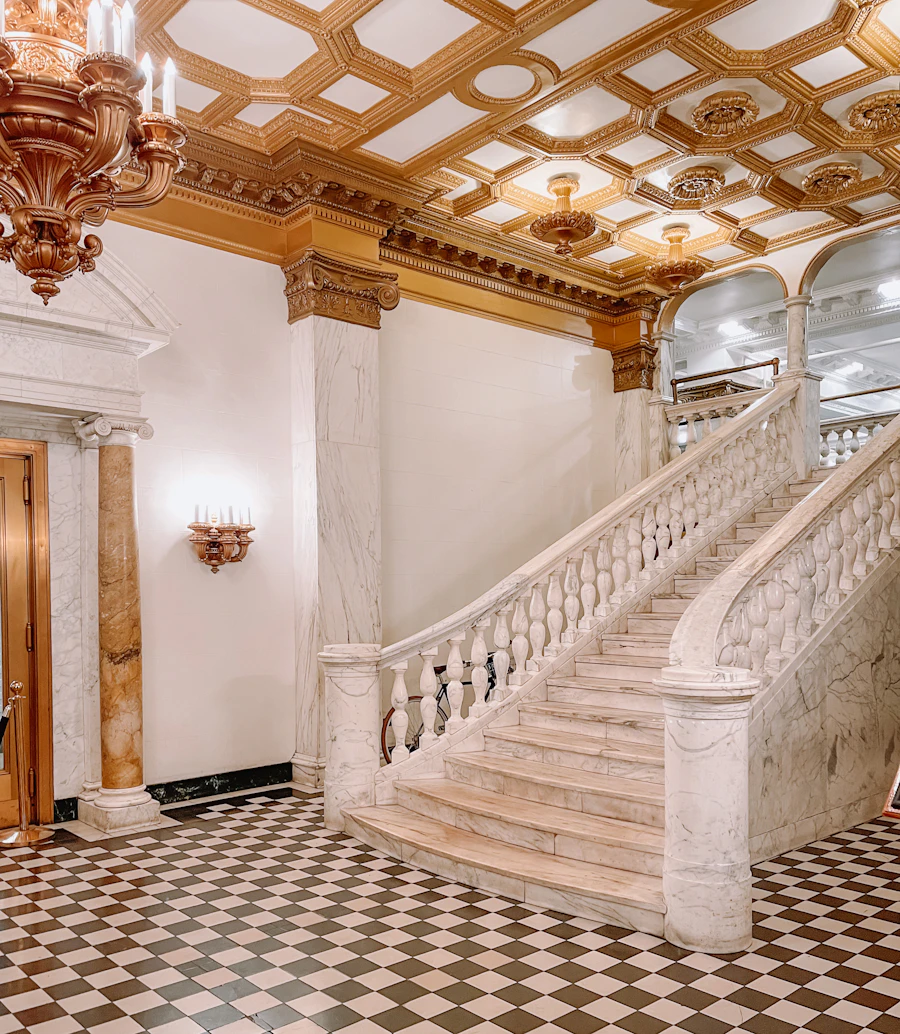 A gilded ceiling and marble staircase in a grand estate entrance hall