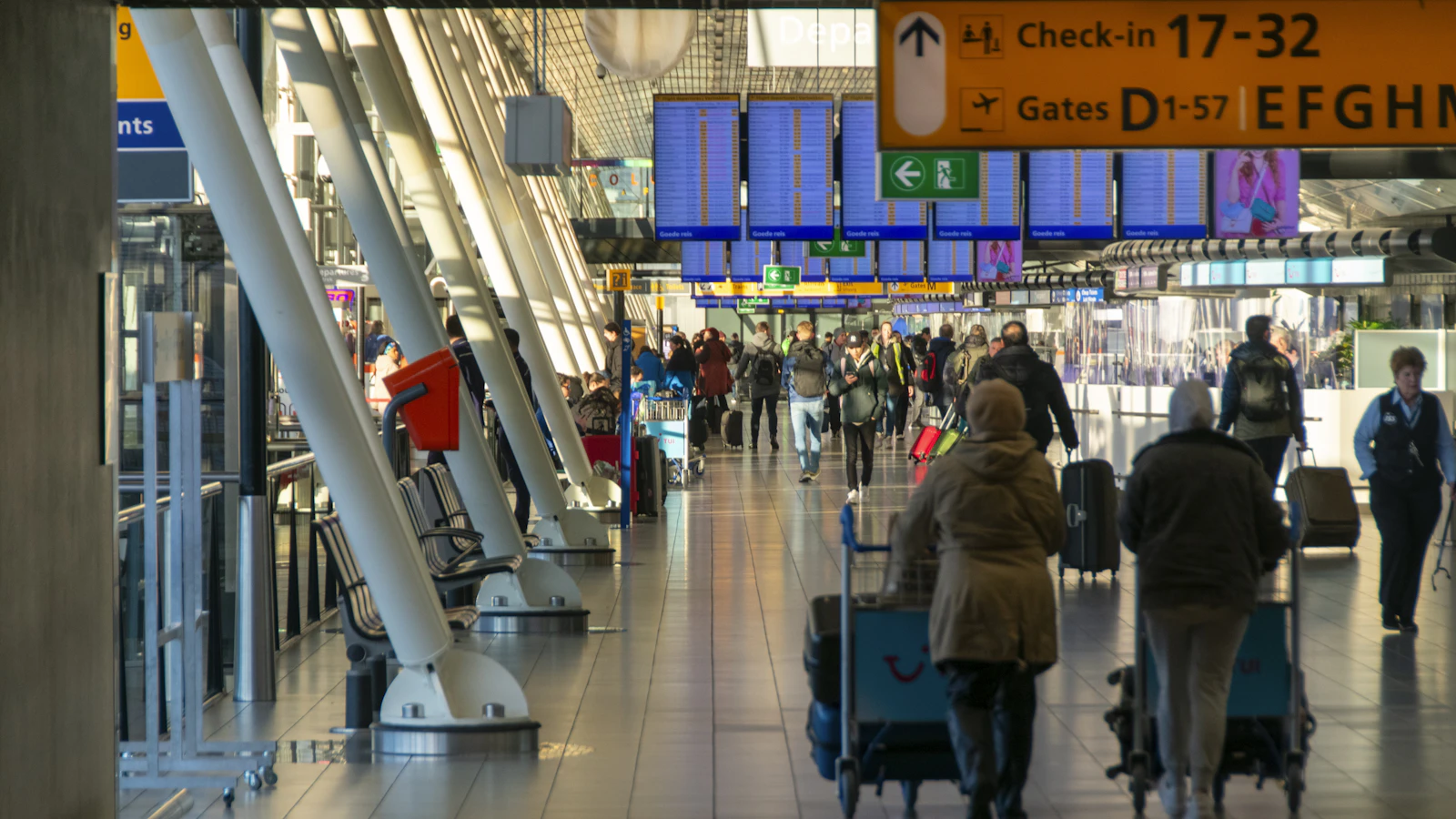 Interior de una terminal aérea con pasajeros caminando hacia las puertas de embarque bajo pantallas de información de vuelos