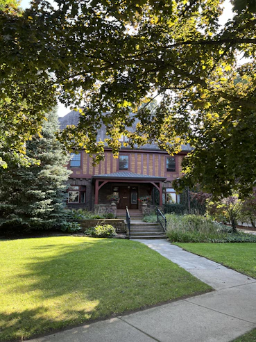 Charming green house with a welcoming front porch and flowering plants.