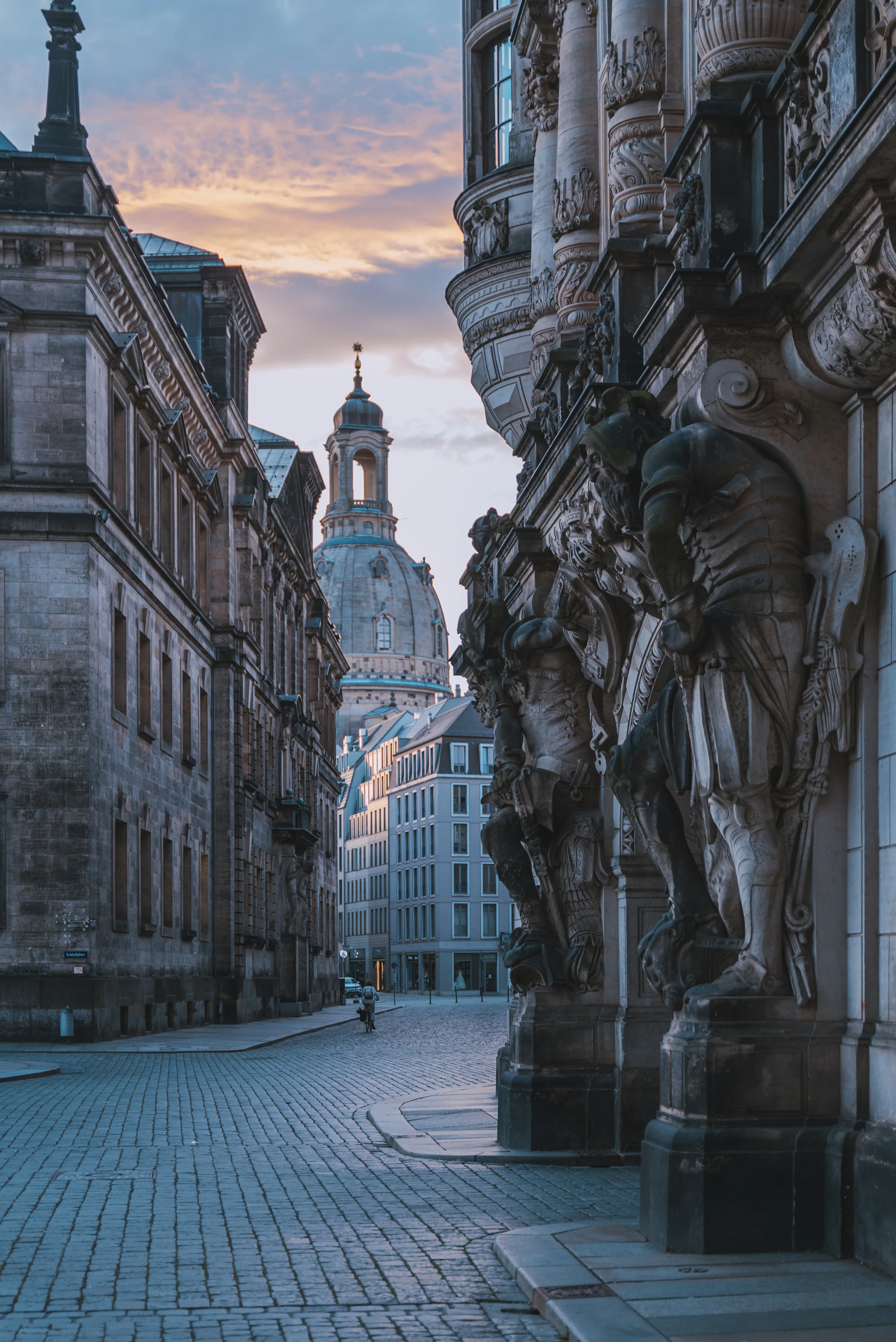a cobblestone street lined with buildings and statues