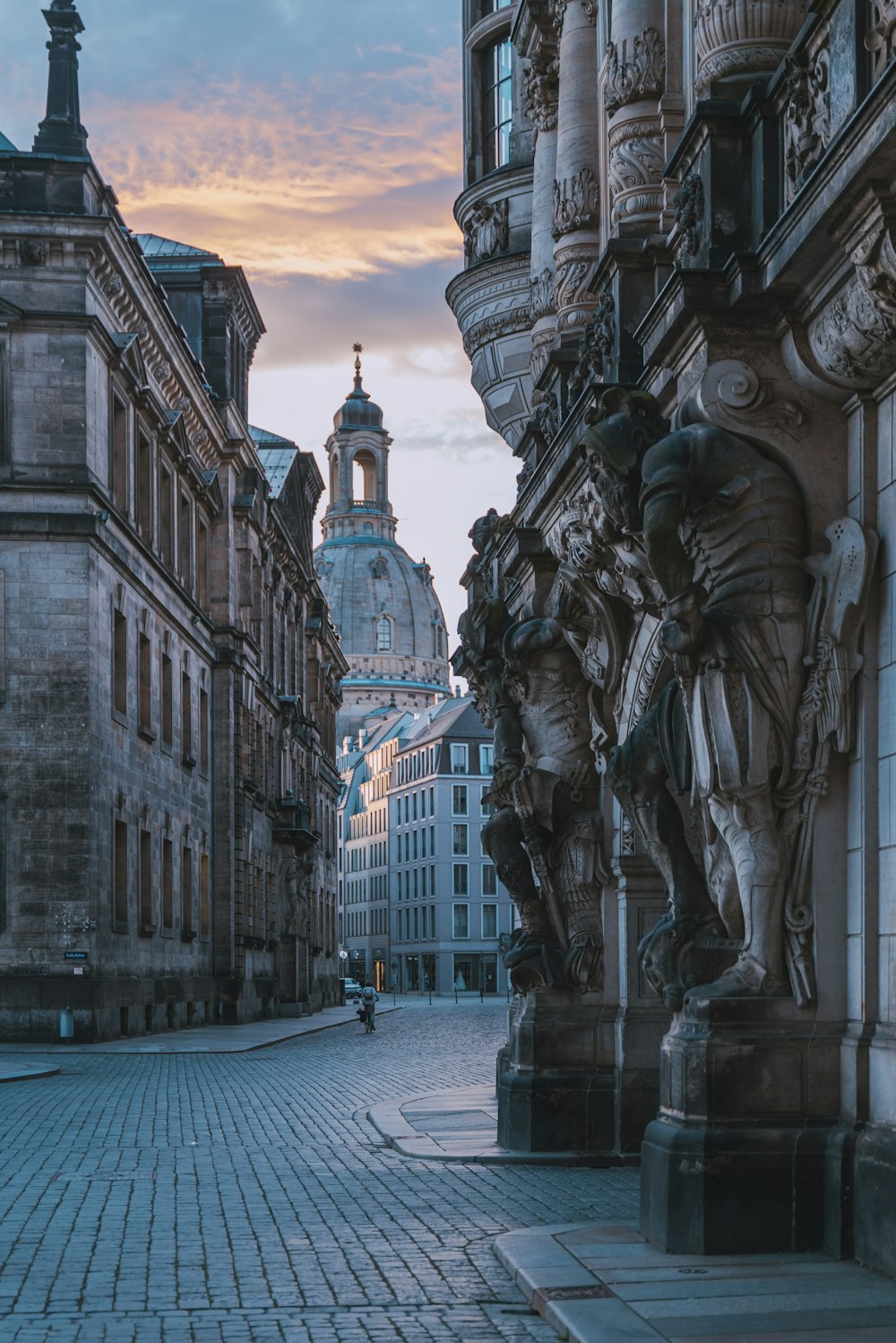 a cobblestone street lined with buildings and statues