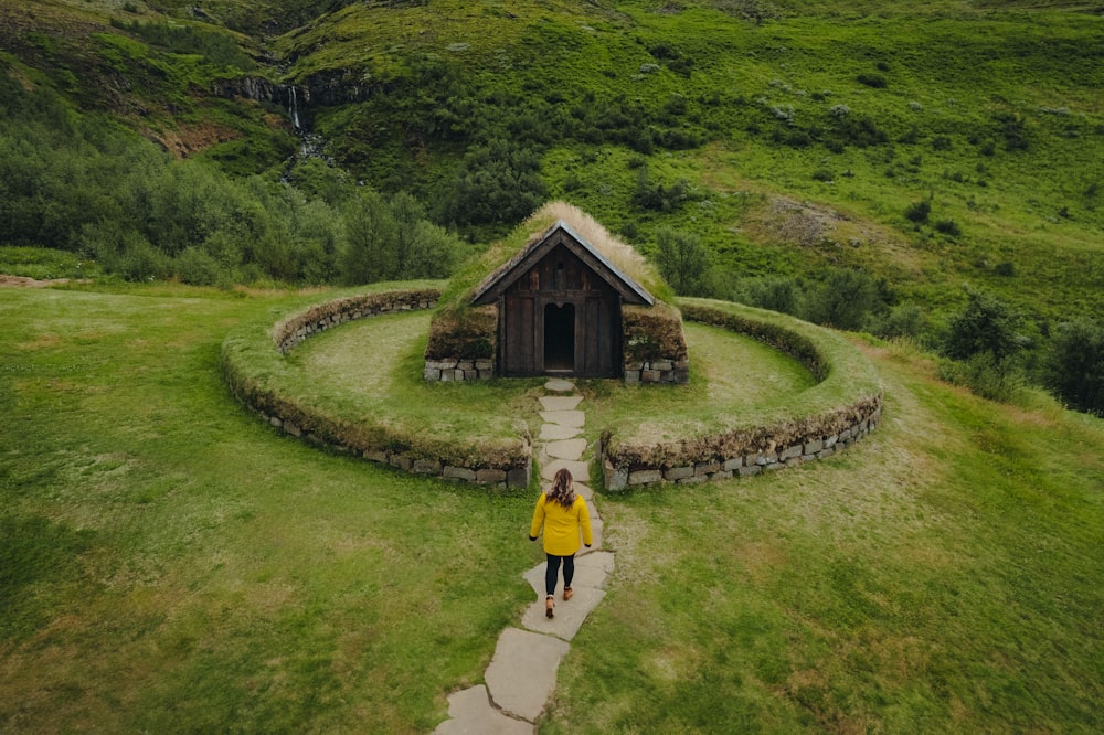 a woman in a yellow jacket is walking towards a small hut