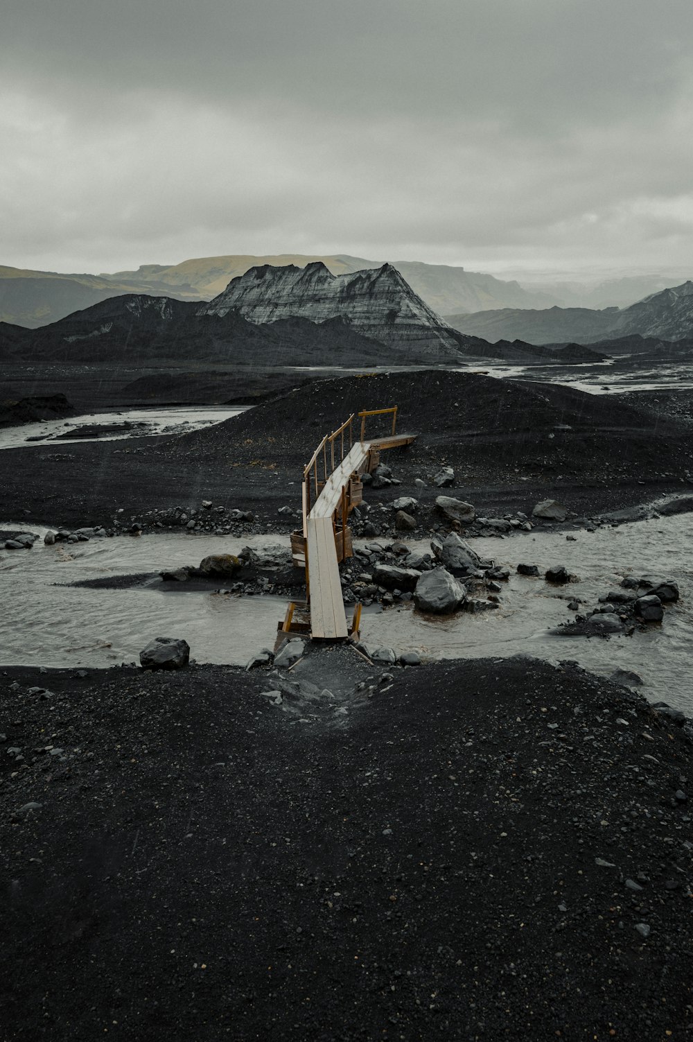 a wooden bridge over a river with mountains in the background