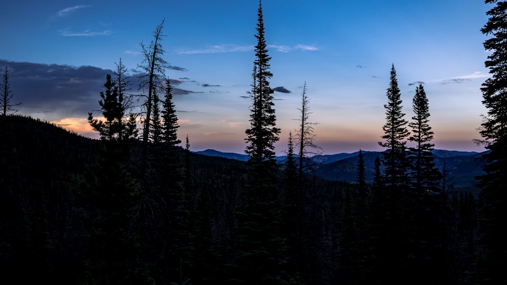 the sun is setting over the mountains and trees