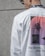 A person is wearing a white shirt featuring abstract designs with red and black elements and the text 'Old Stories... New Times.' The shirt also includes repetitive text 'THE LAST FEELINGS' along the design. The person is wearing sunglasses and has a floral pattern on the collar of a shirt visible underneath.